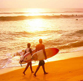 Couple of surfers walks along the beach in Hikkaduwa